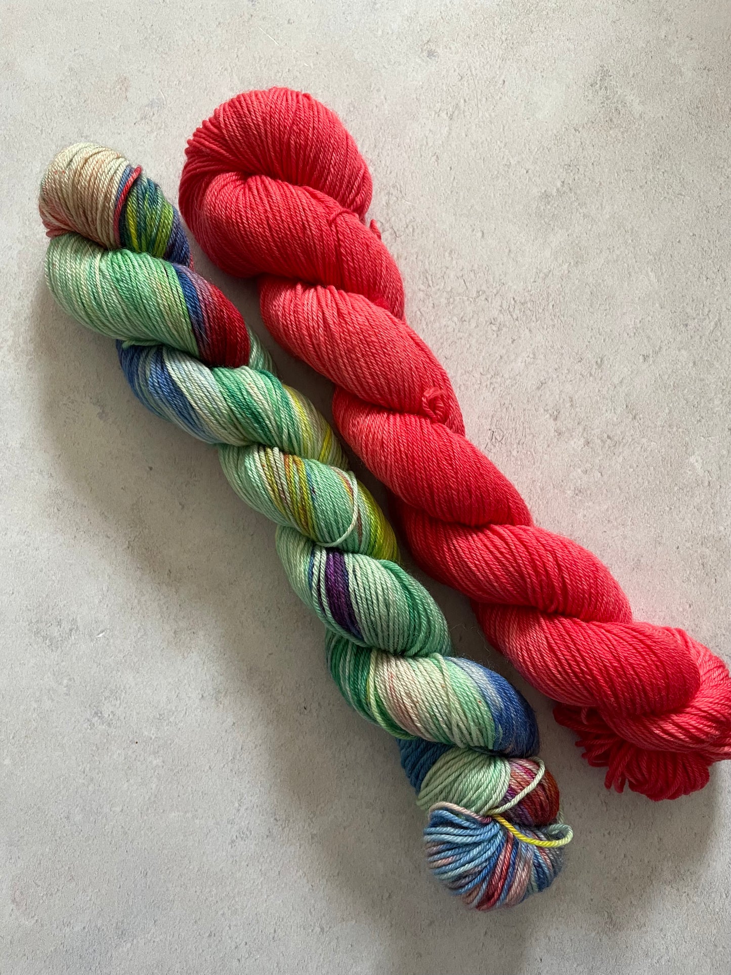 One 50g variegated green and multicoloured skein and one 50g red skein