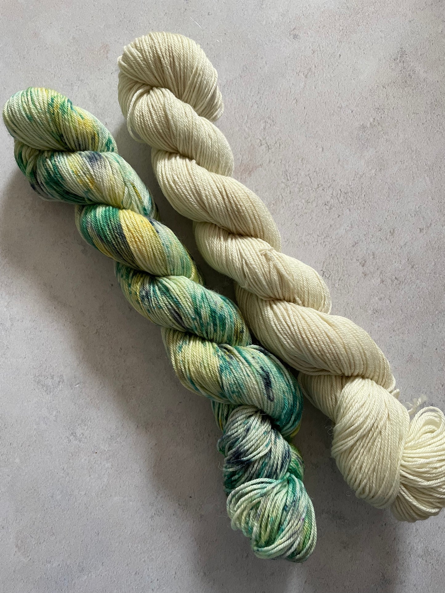 One 50g variegated green yellow and black skein and one 50g cream pink skein
