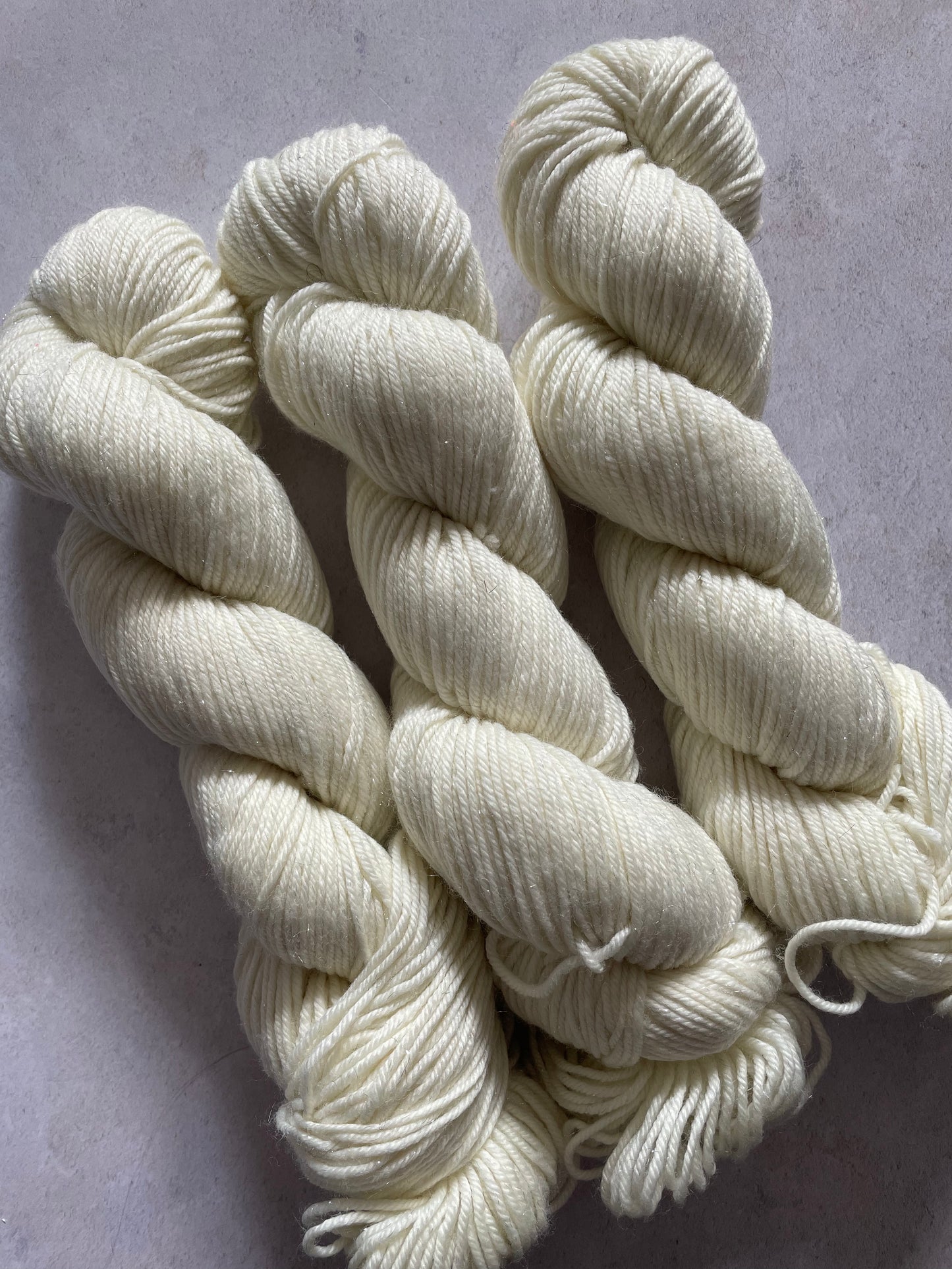 Three skeins of undyed silver sparkle double knitting yarn