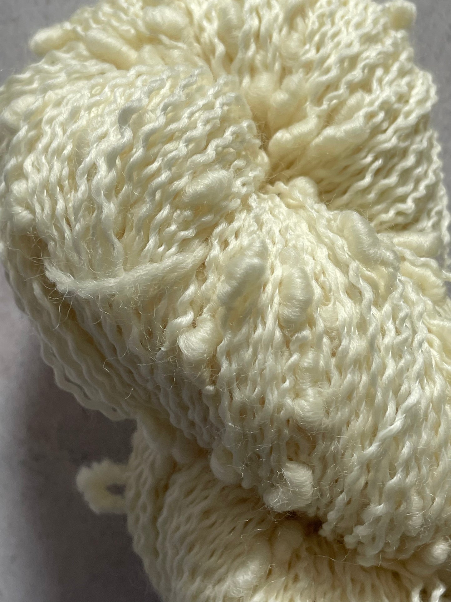 A close up of slub cream yarn with a wiggly bumpy texture