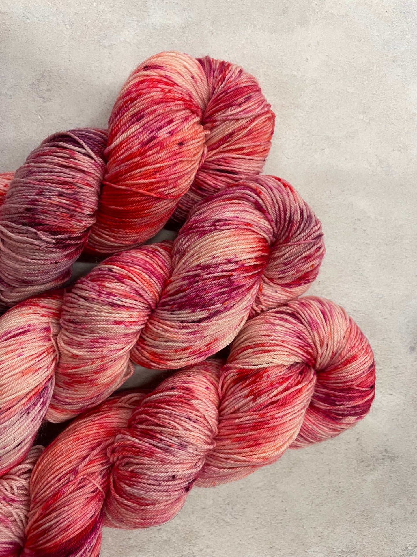 3 skeins of hand dyed sock yarn featuring shades of red, pink and purple
