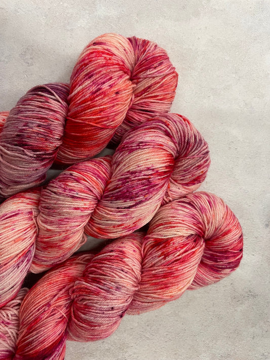 3 skeins of hand dyed sock yarn featuring shades of red, pink and purple