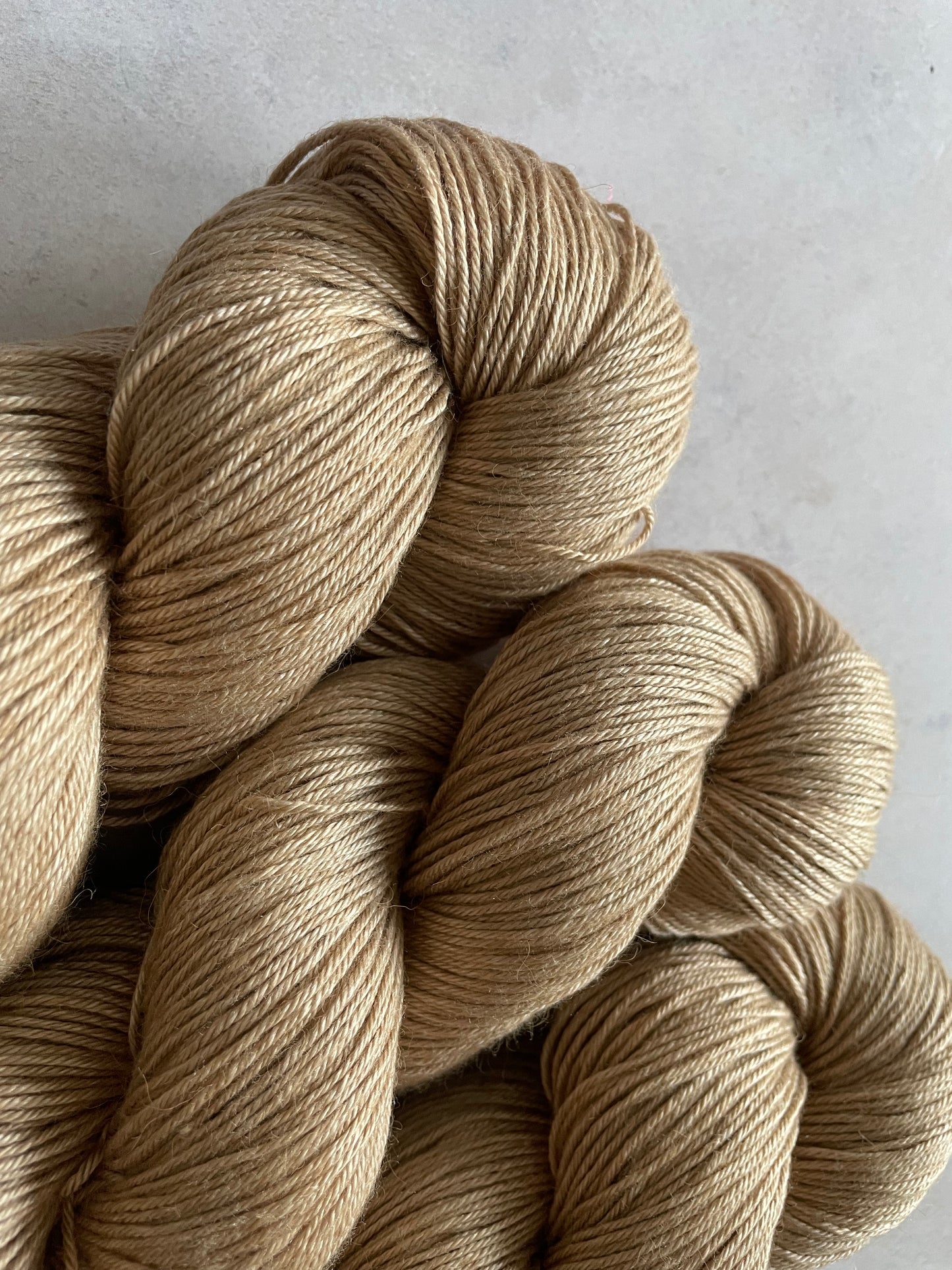 Close up of 3 skeins of camel and silk 4ply weight yarn with a light warm brown tone