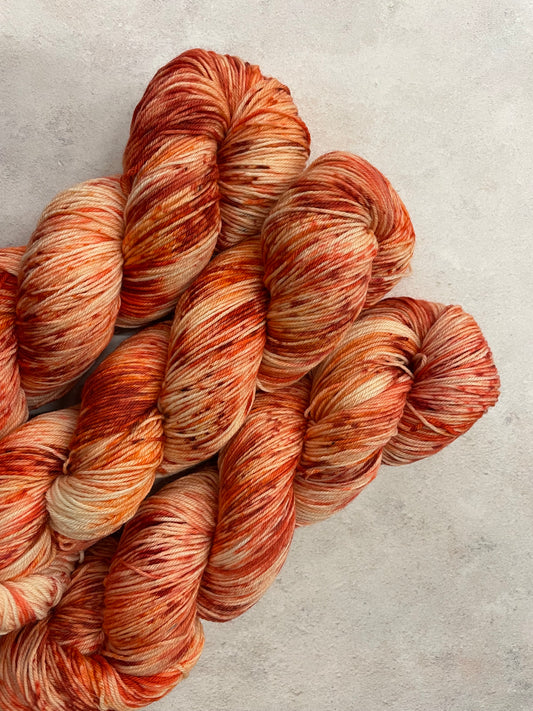 3 skeins of hand dyed sock yarn featuring shades of orange, red and coral