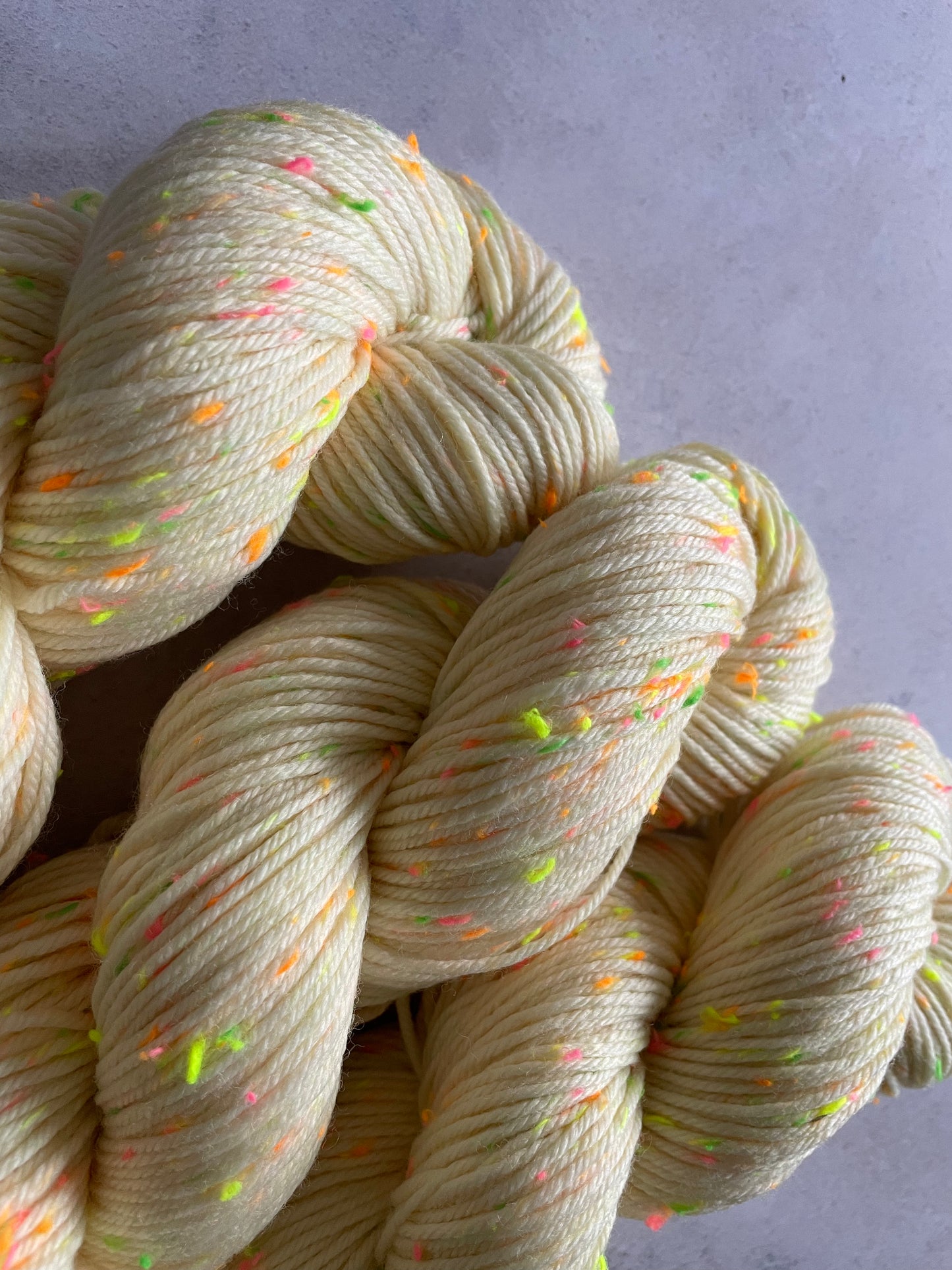Close up of 3 skeins of cream double knitting yarn with neon green pink and orange and yellow neps