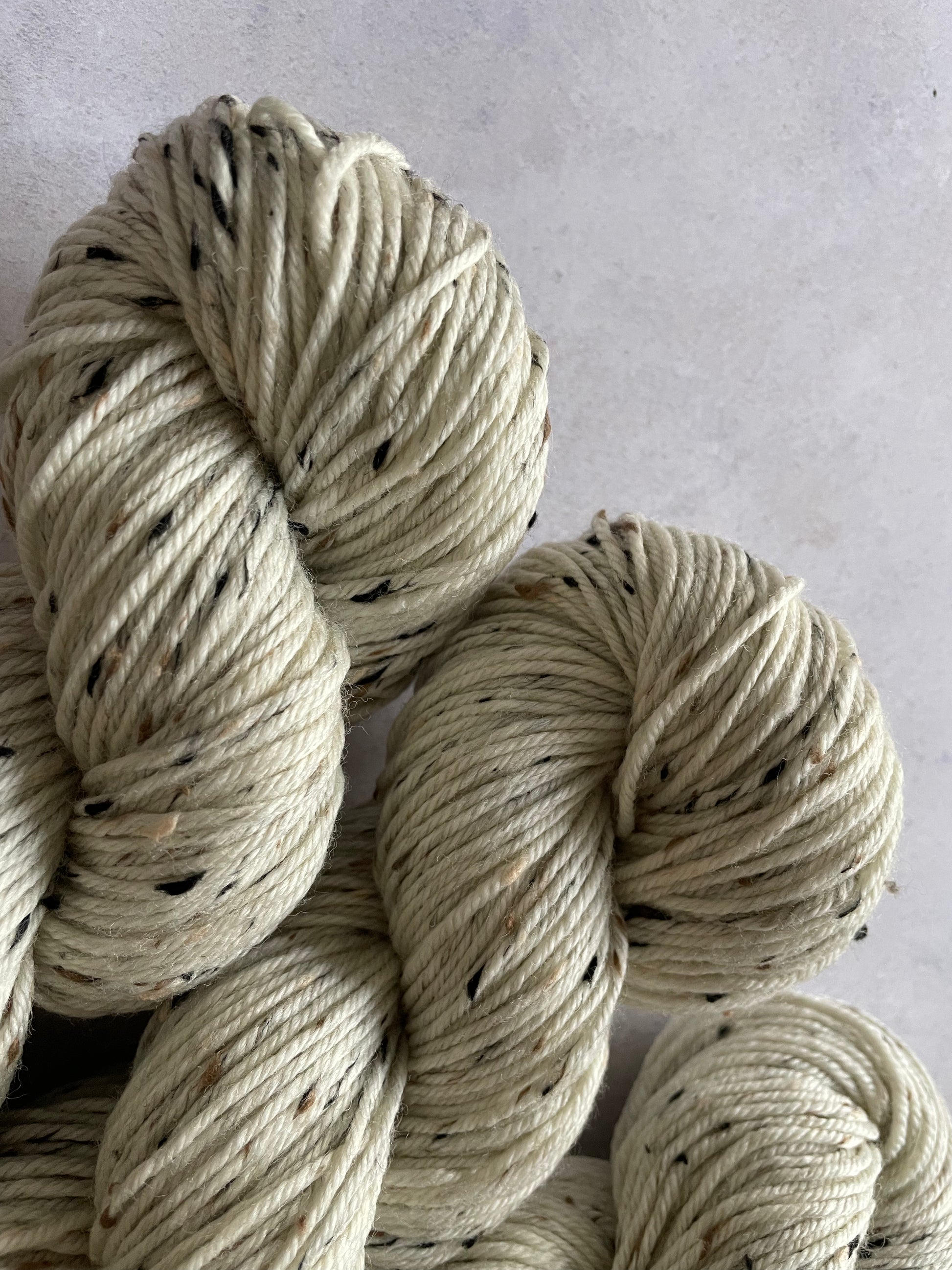 Close up of 3 skeins of cream double knitting yarn with black and tan neps