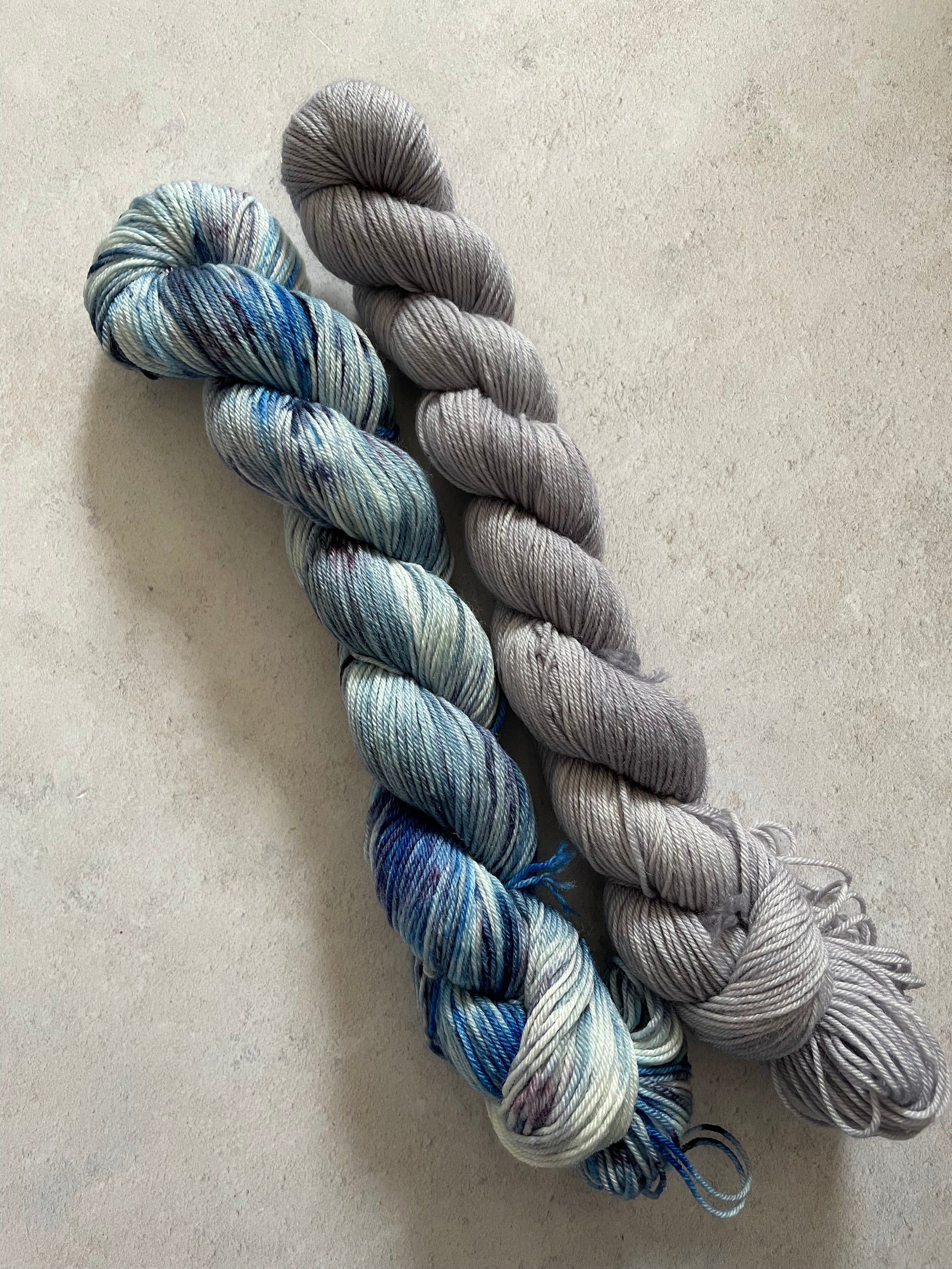 One 50g variegated blue purple and grey skein and one 50g grey skein