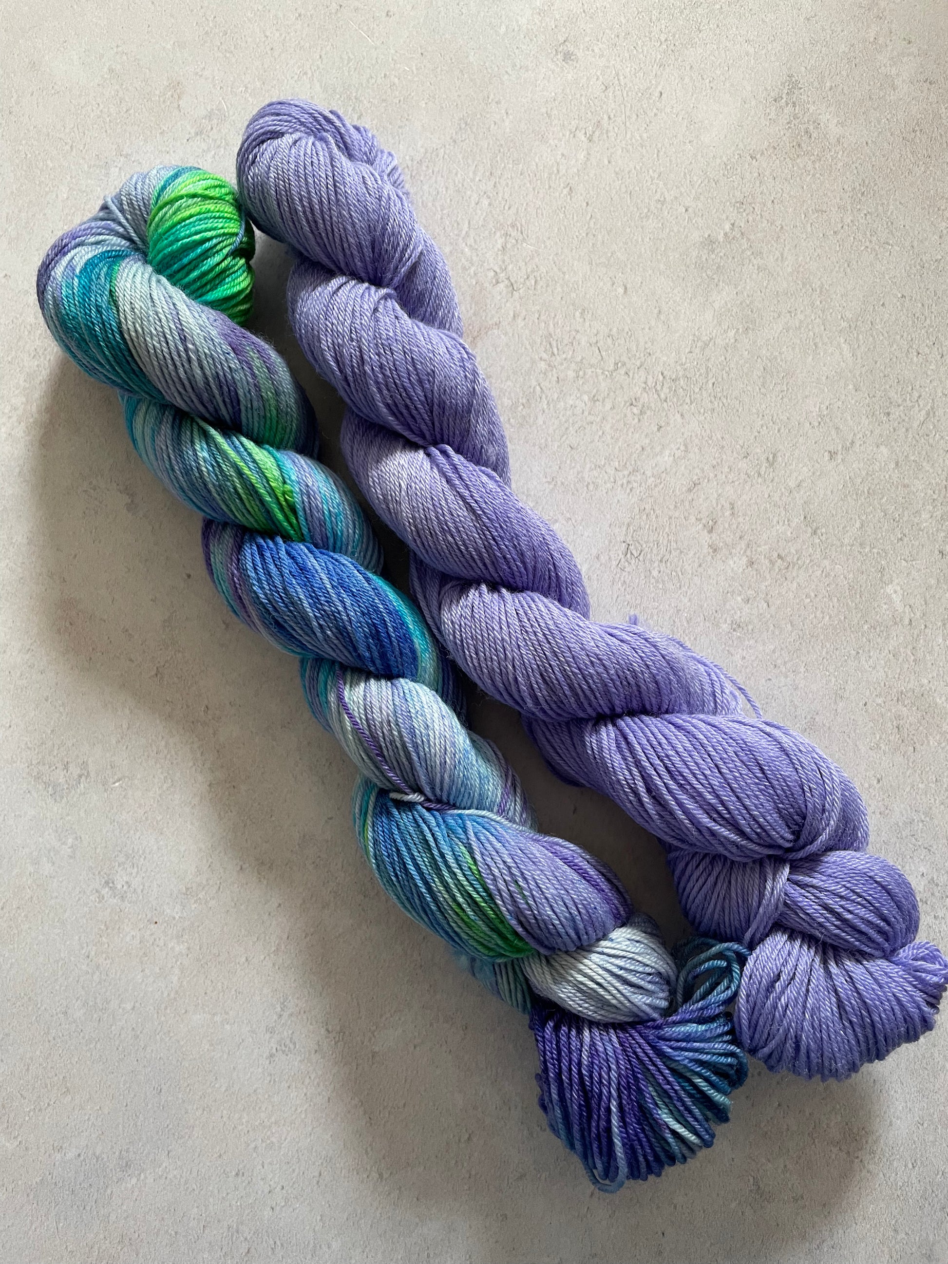 One 50g variegated purple green and blue skein and one 50g purple skein