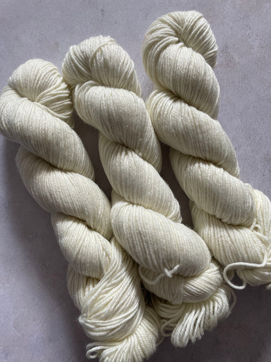Three skeins of undyed silver sparkle double knitting yarn