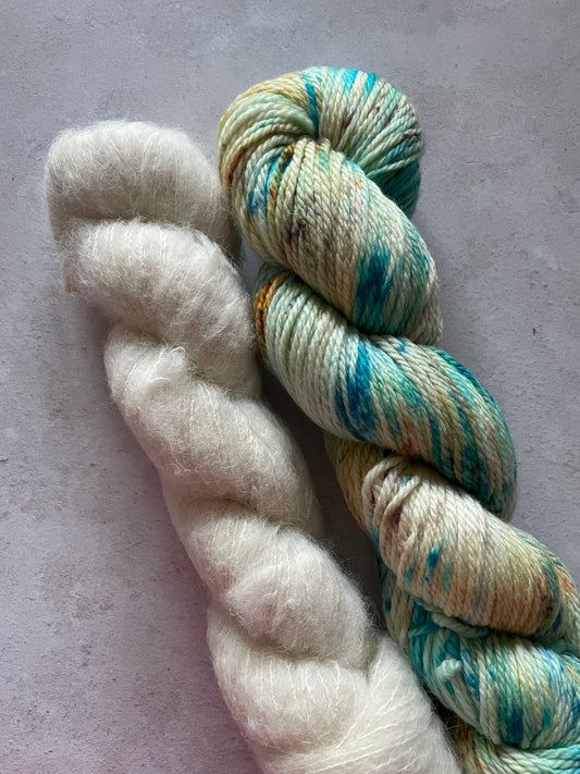 a skein of fluffy suri alpaca and silk yarn and a skein of double knitting yarn with blue and gold