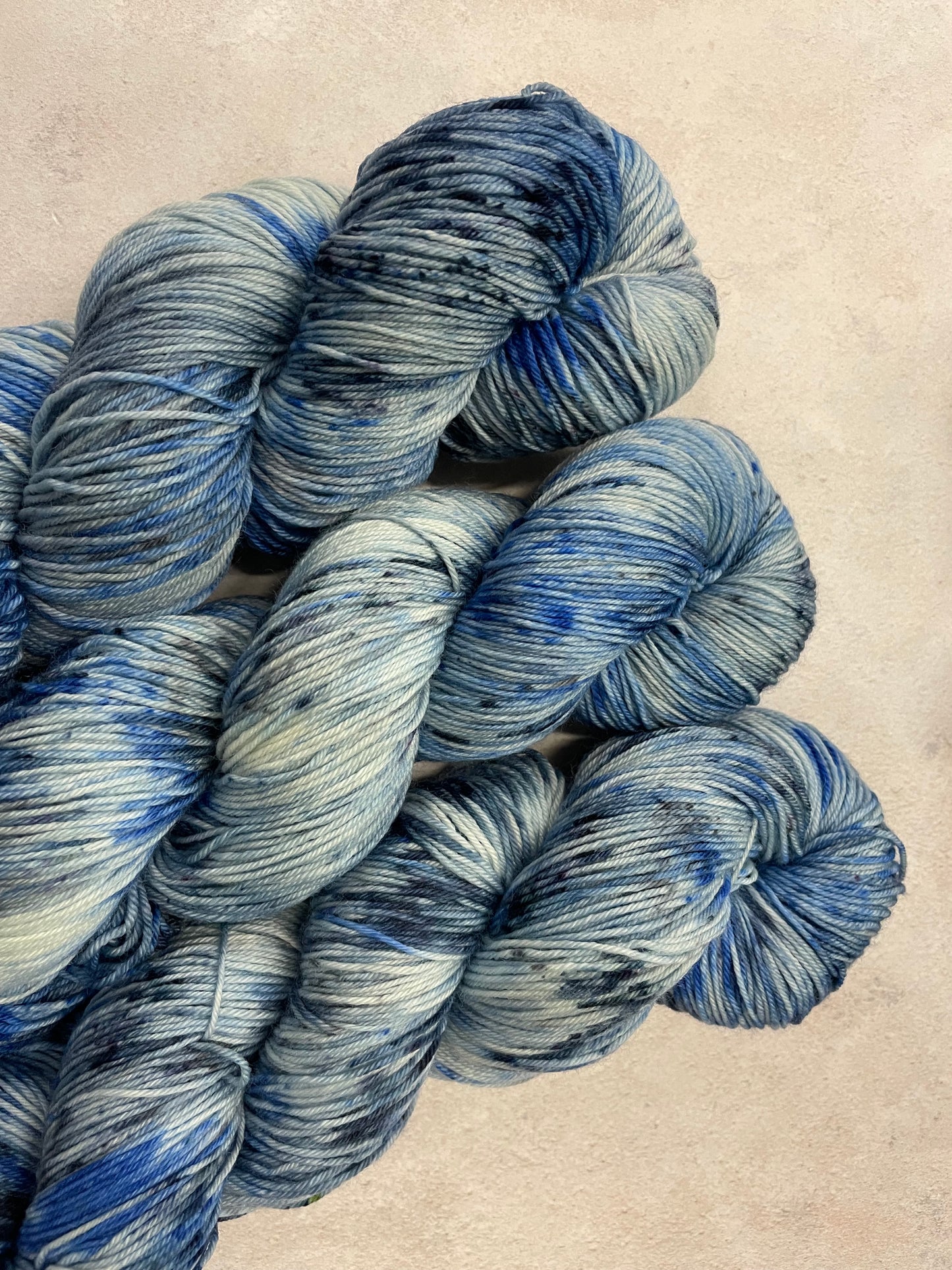 3 skeins of hand dyed sock yarn featuring shades of blue, grey and navy