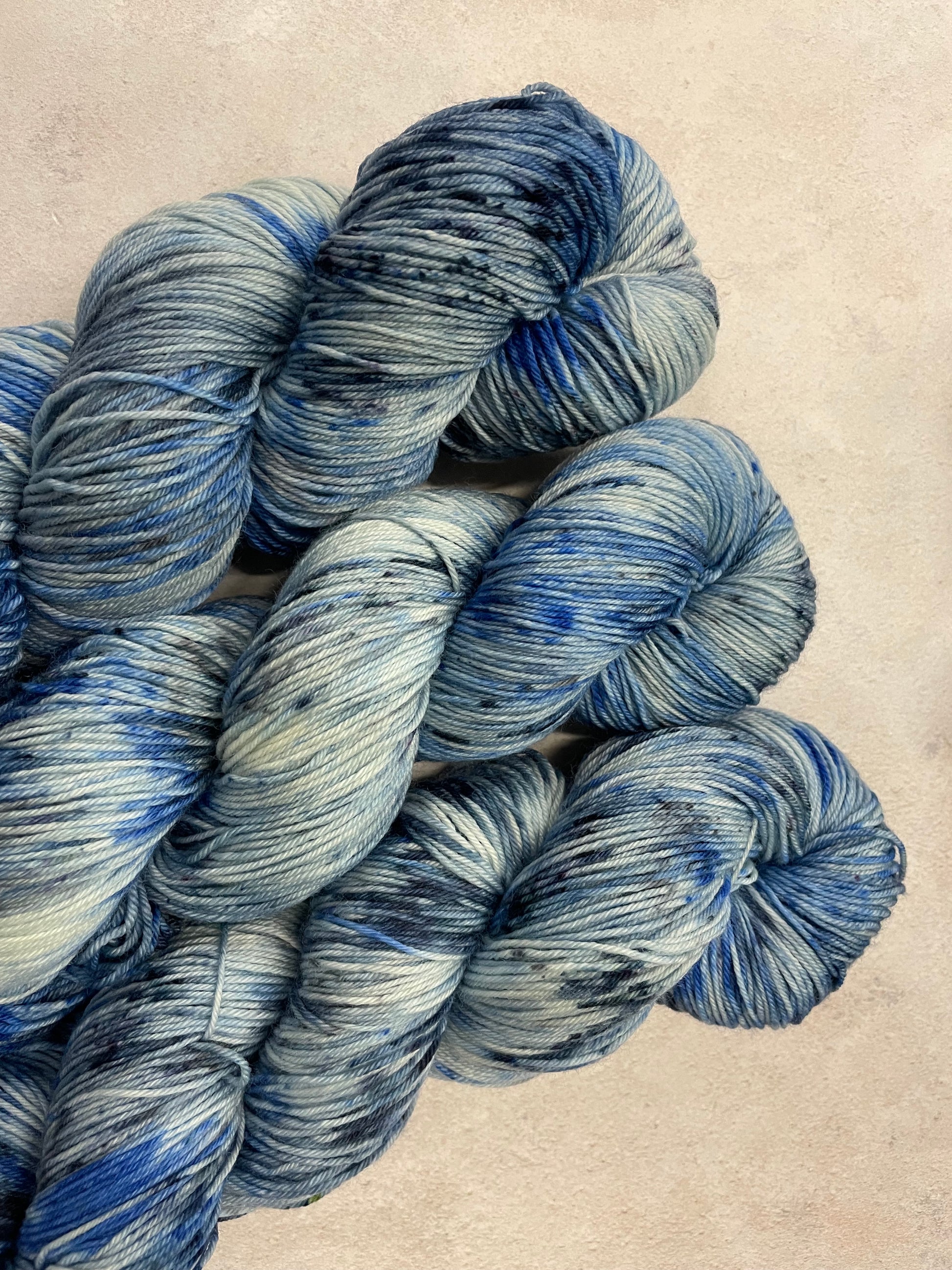3 skeins of hand dyed sock yarn featuring shades of blue, grey and navy
