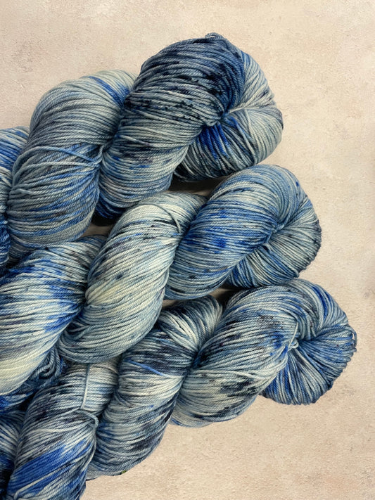 3 skeins of hand dyed sock yarn featuring shades of blue, grey and navy
