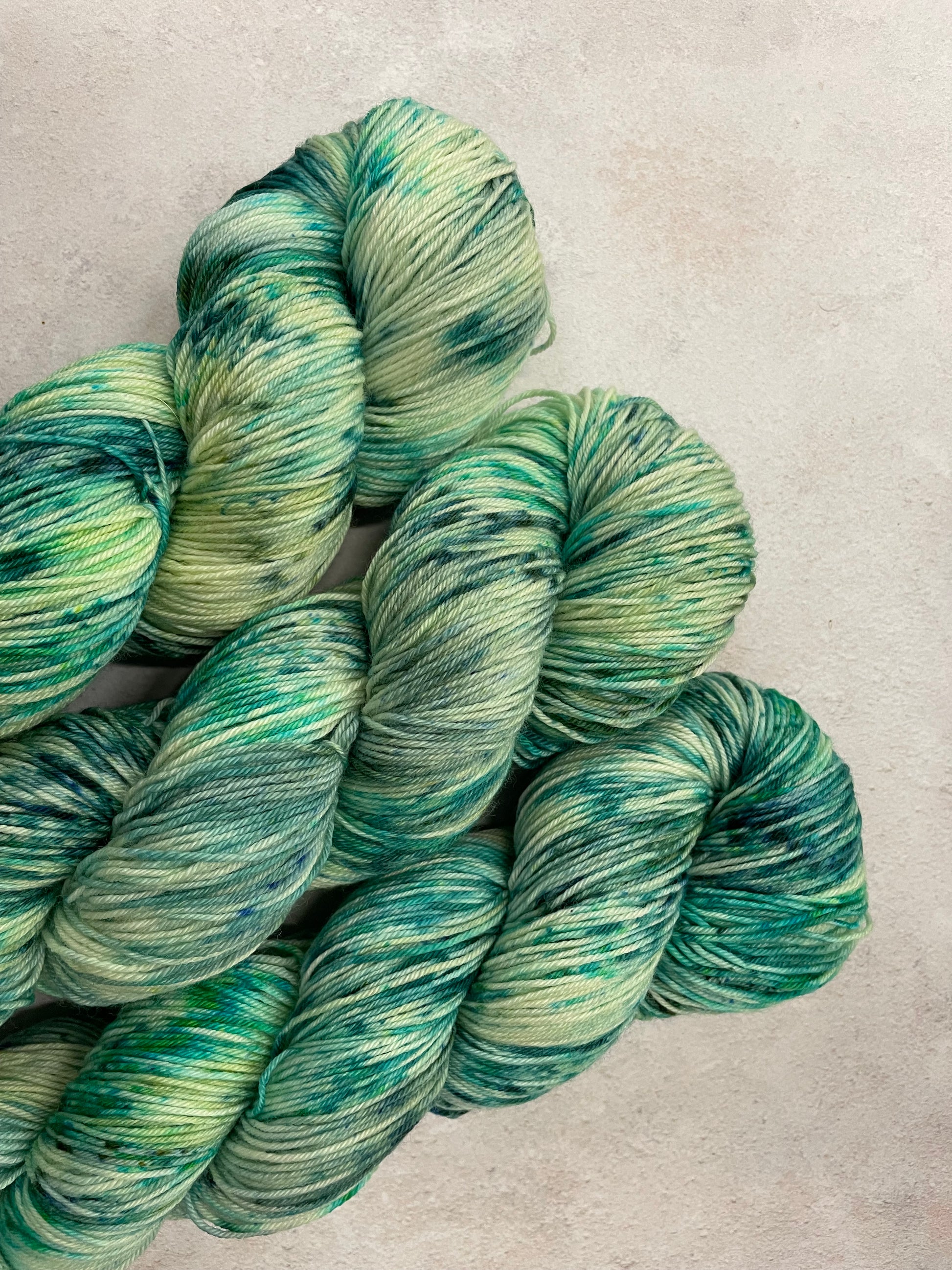 3 skeins of hand dyed sock yarn featuring shades of green and teal