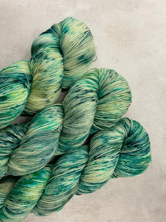 3 skeins of hand dyed sock yarn featuring shades of green and teal