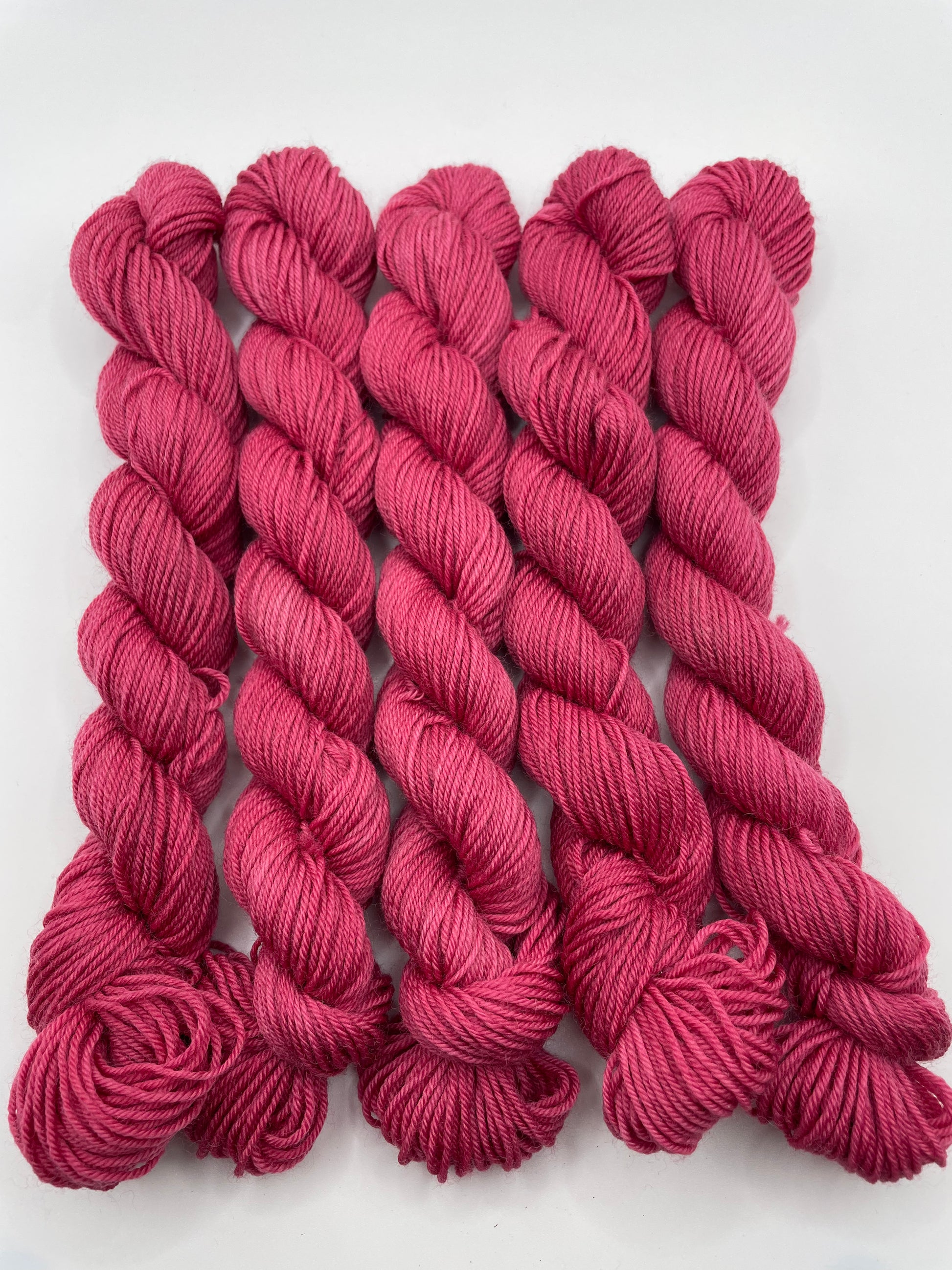 Deep pink yarn mini skeins on a white background
