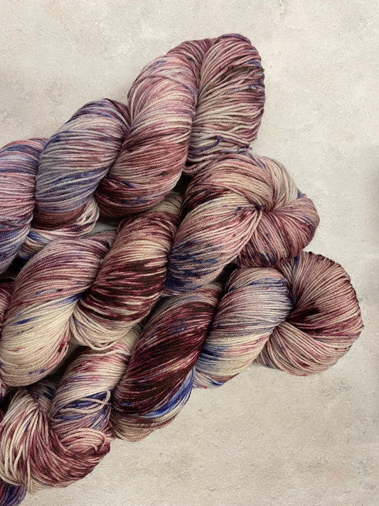 3 skeins of hand dyed sock yarn featuring shades of burgundy, violet and lilac
