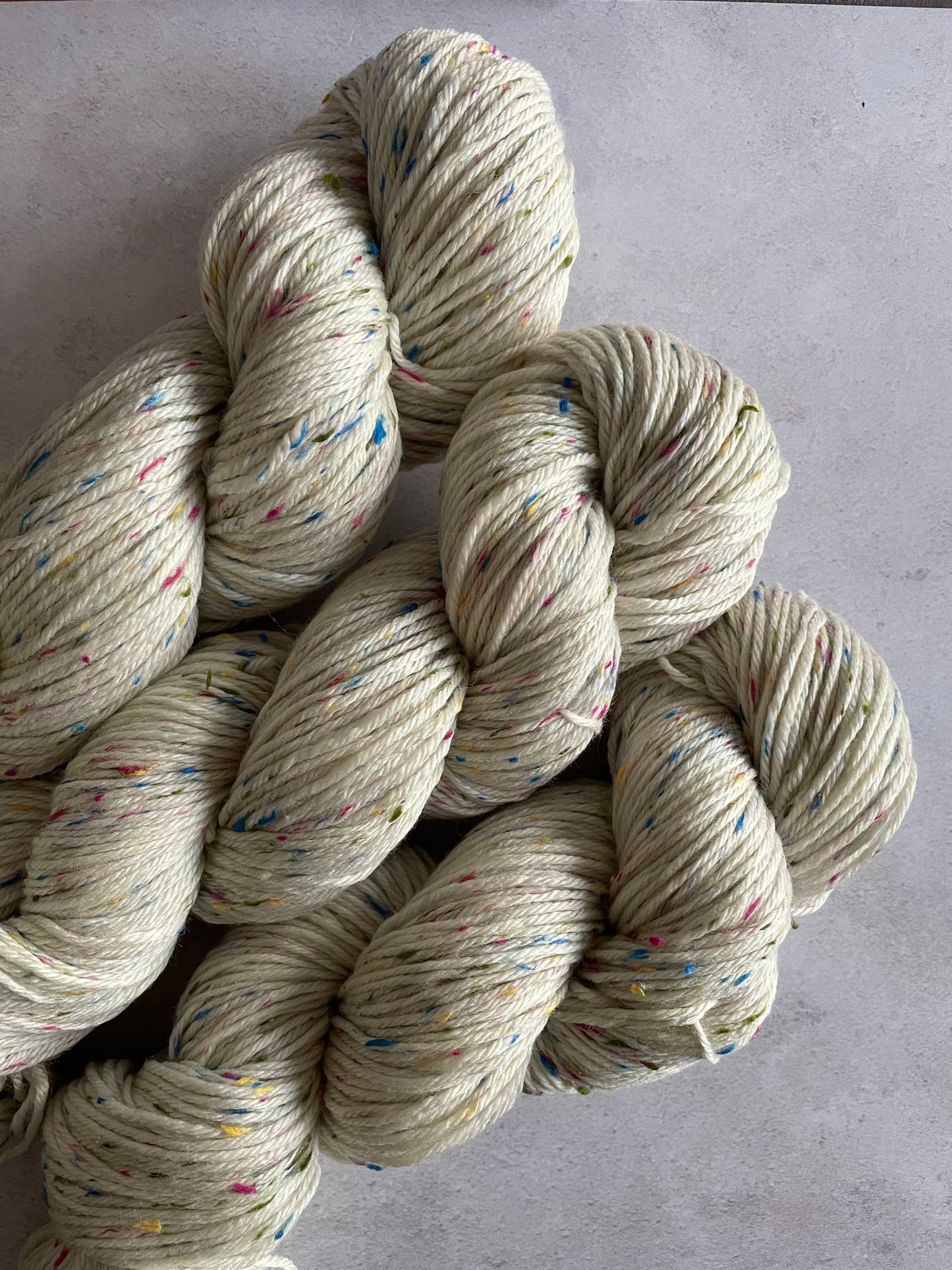 3 skeins of neutral double knitting yarn with green pink and blue neps