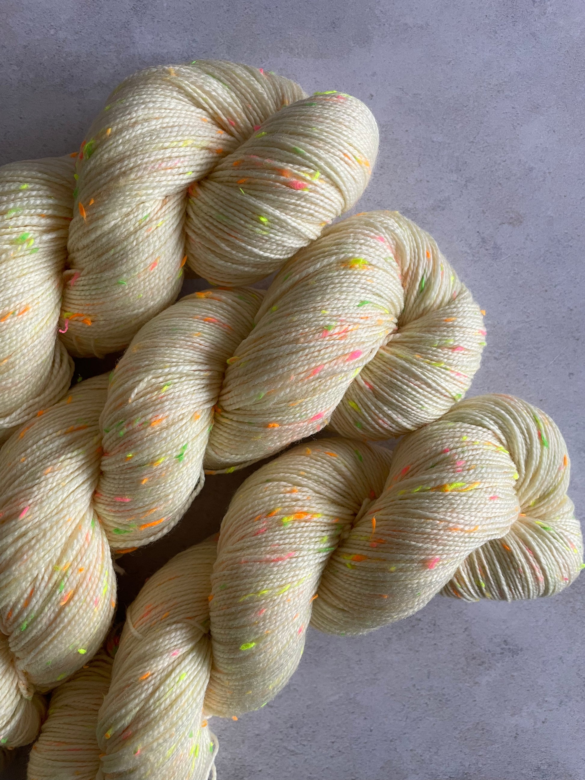 3 skeins of cream 4ply weight yarn with neon green pink and orange and yellow neps