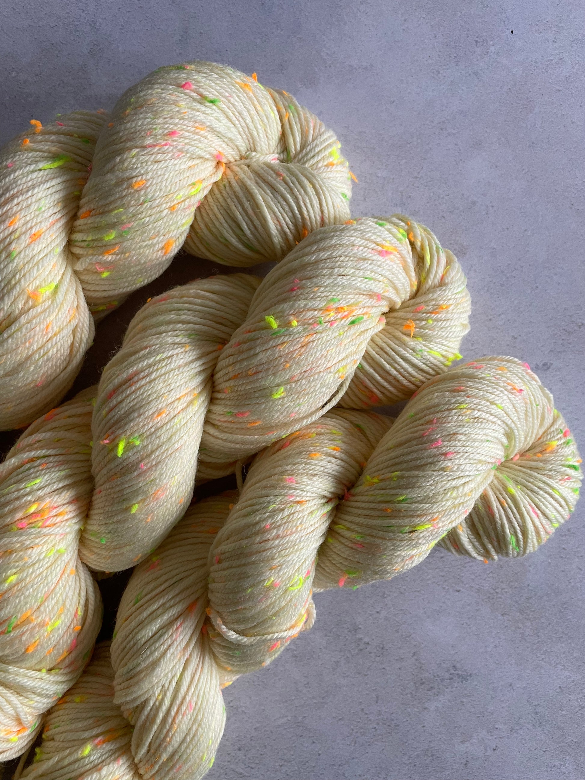 3 skeins of cream double knitting yarn with neon green pink and orange and yellow neps