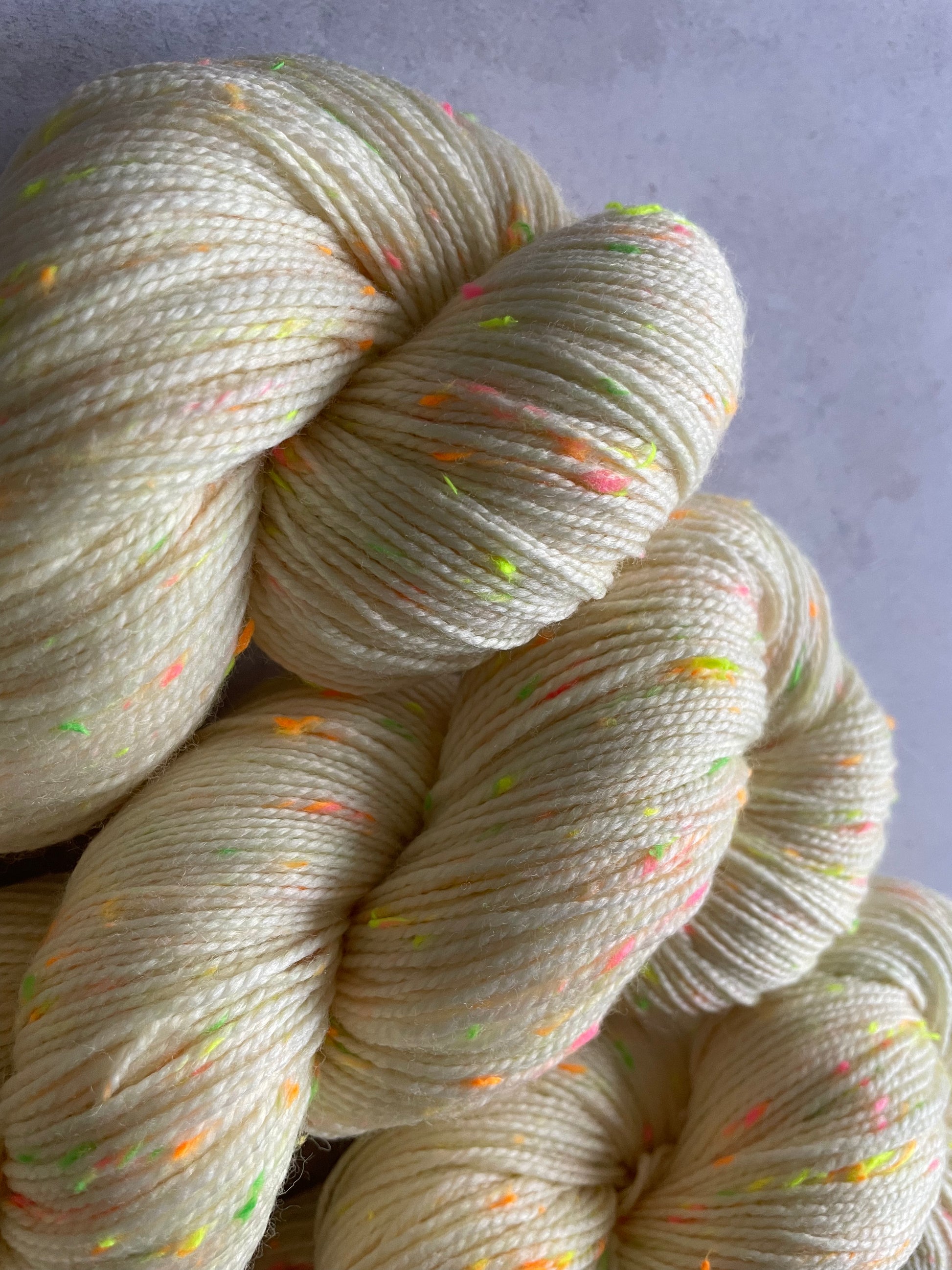Close up of 3 skeins of cream 4ply weight yarn with neon green pink and orange and yellow neps
