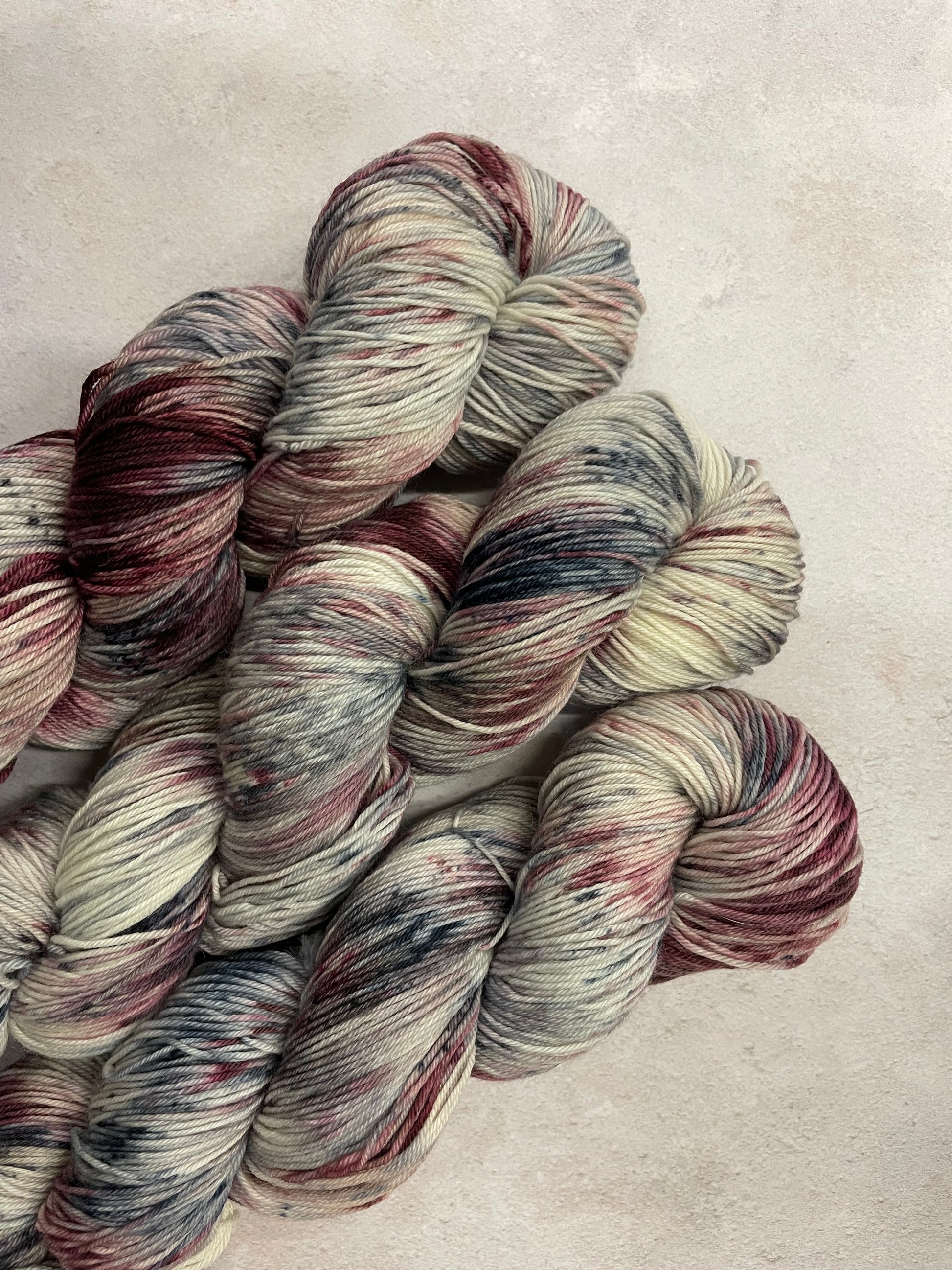 3 skeins of hand dyed sock yarn featuring shades of grey, burgundy and charcoal
