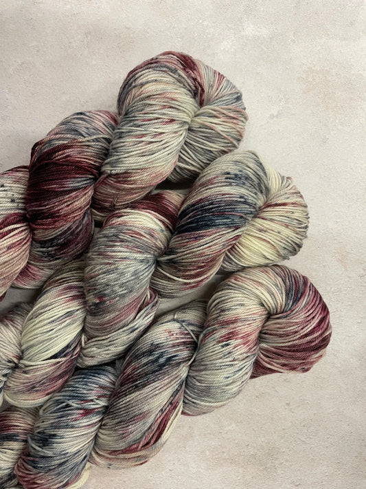 3 skeins of hand dyed sock yarn featuring shades of grey, burgundy and charcoal