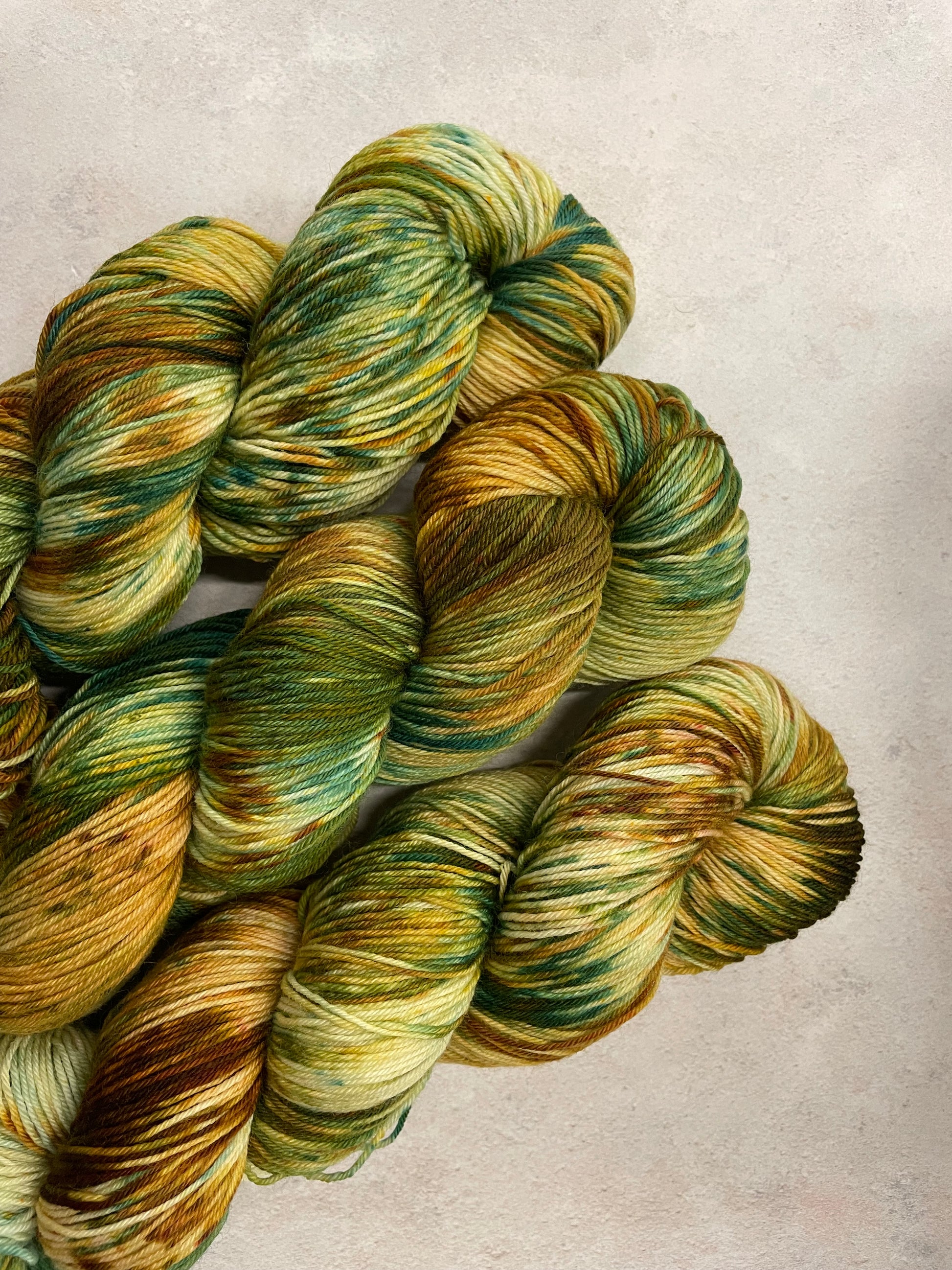 3 skeins of hand dyed sock yarn featuring shades of green, gold and brown