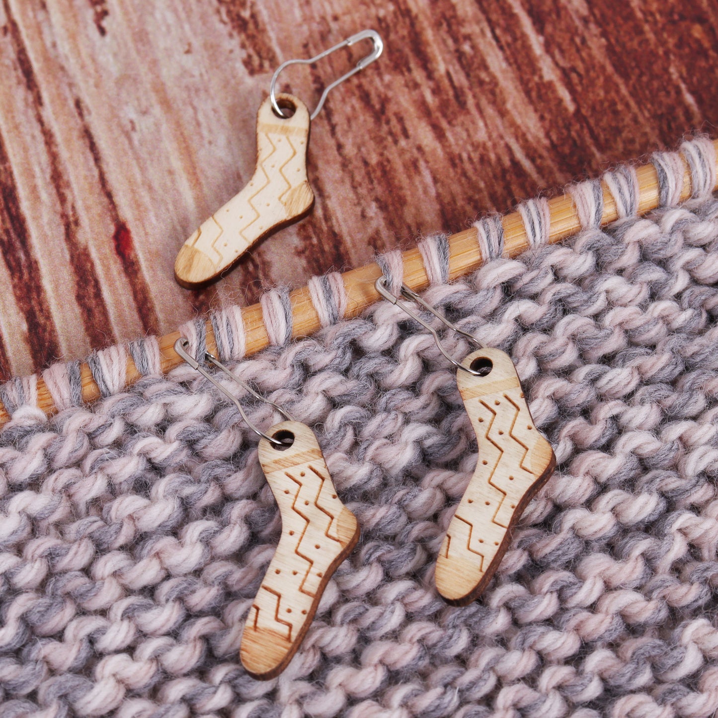 Three wooden sock stitch markers on a wooden and knitted background