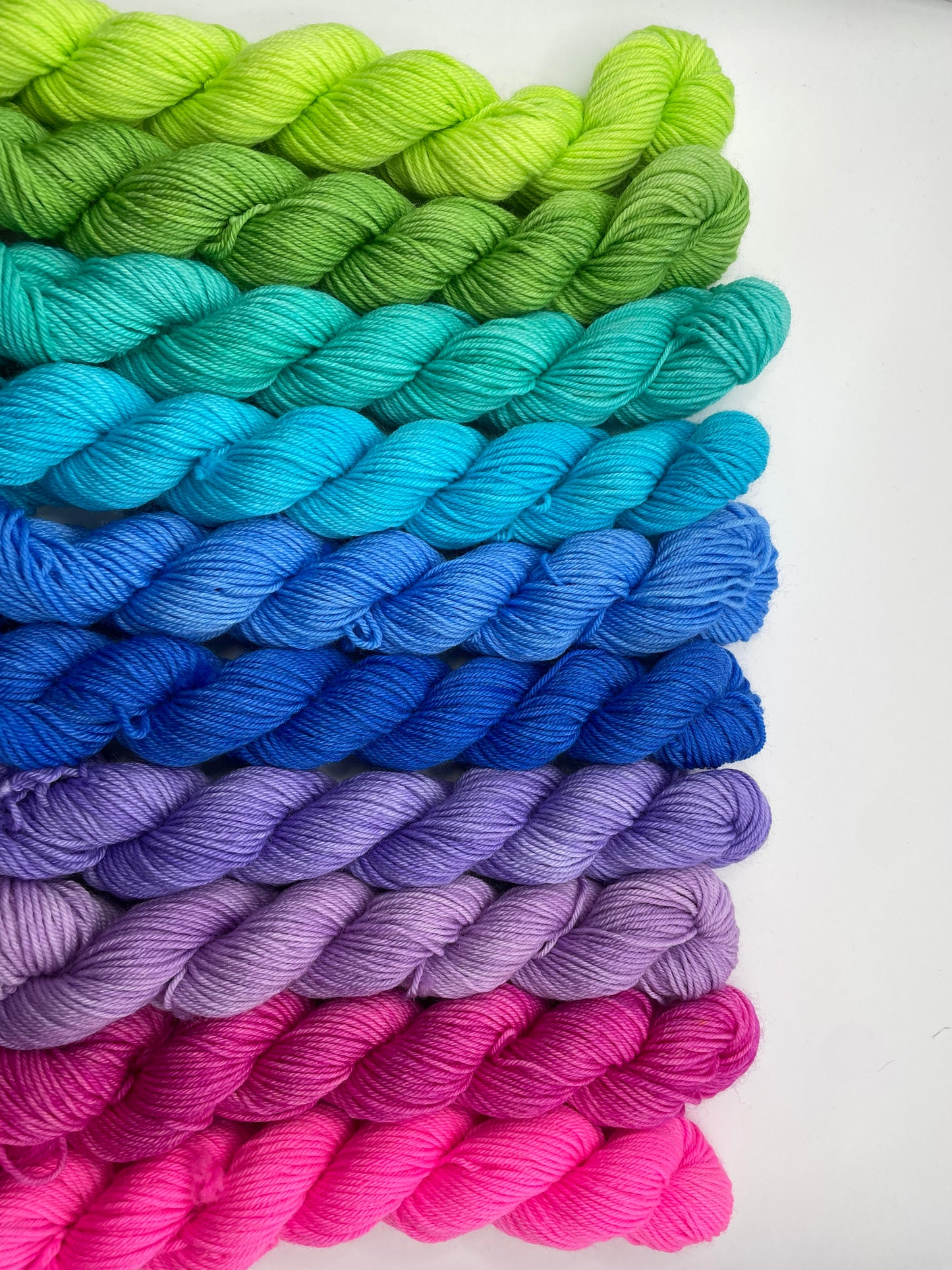 Colorful yarn skeins arranged in a gradient from green to pink on a white background
